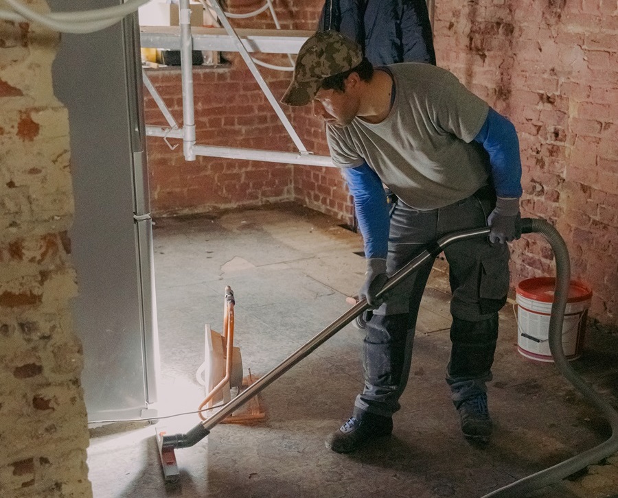 A young man vacuums the landing in a repair room.
