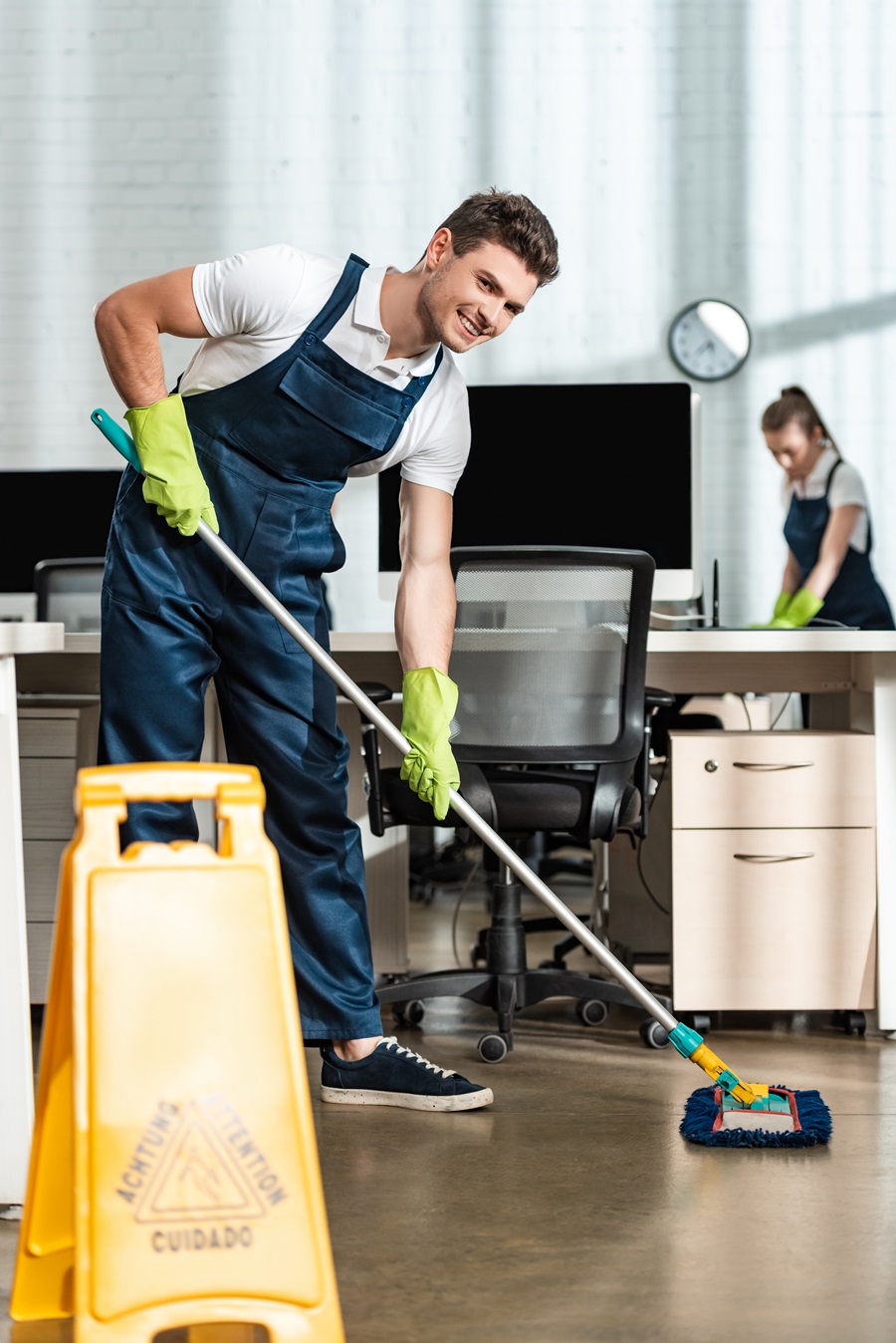 cheerful cleaner washing floor with mop while smiling at camera