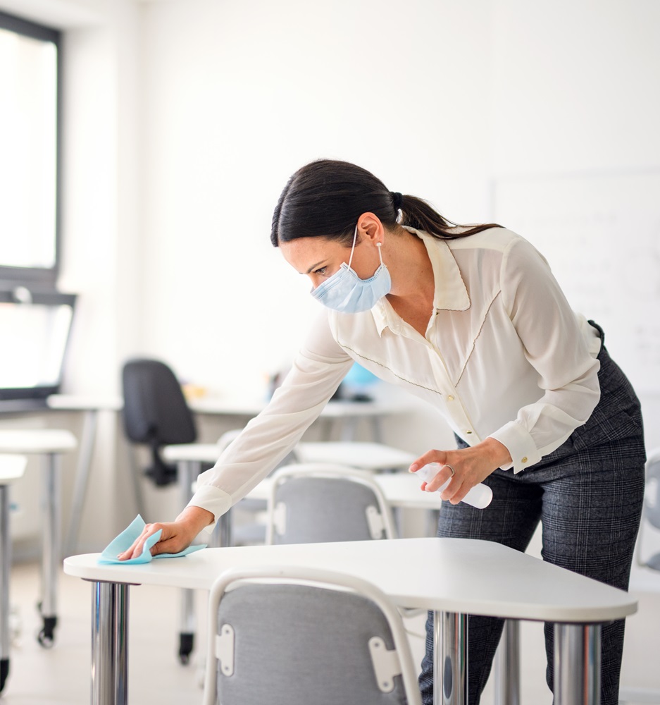 Teacher back at school after covid-19 quarantine and lockdown, disinfecting desks.