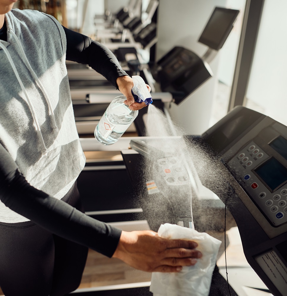 Unrecognizable athlete disinfecting treadmill after sports training at health club.